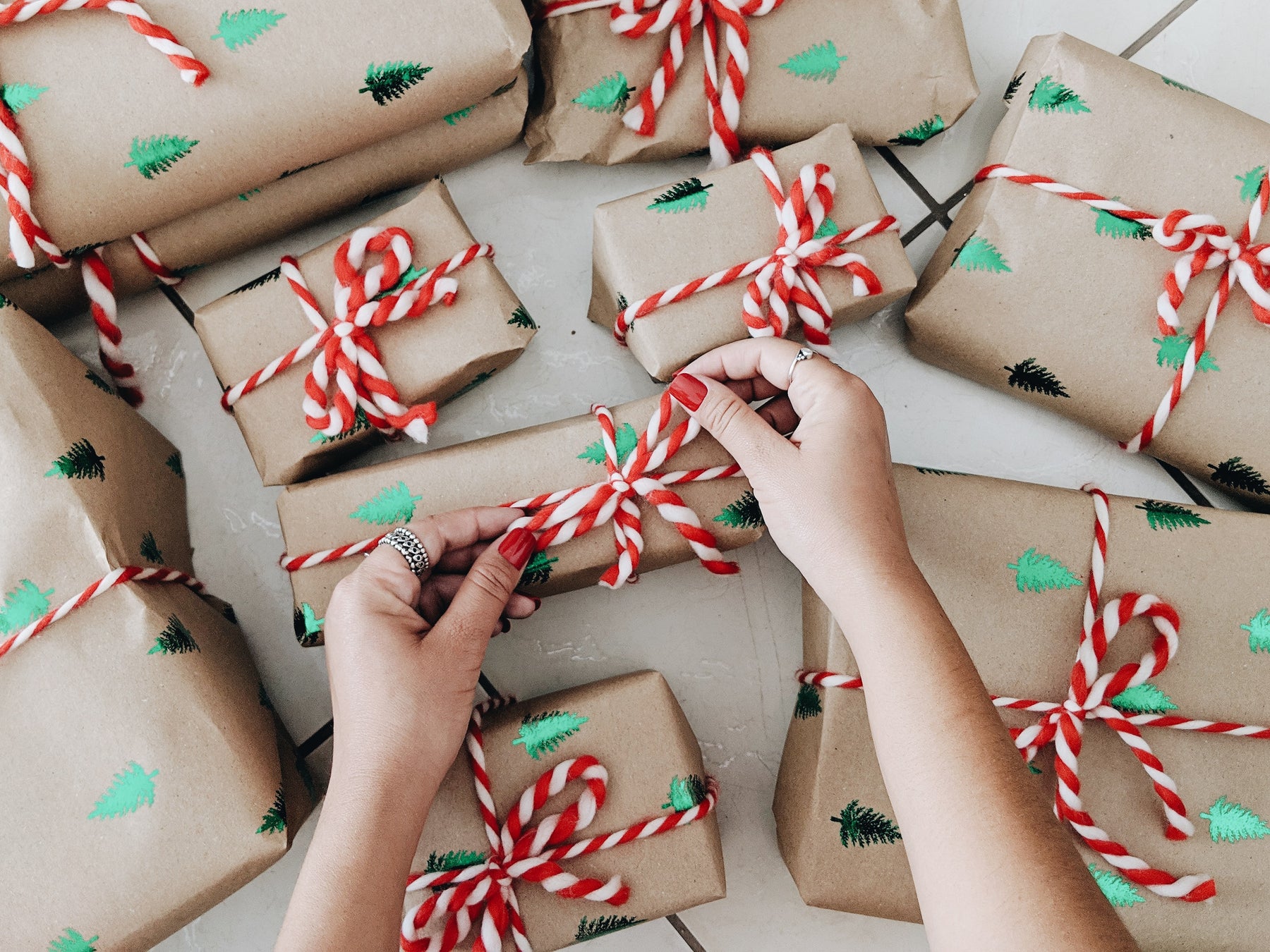 person wrapping christmas gifts. wrapping paper is tan coloured with green foil trees and tied up with candy cane patterned string